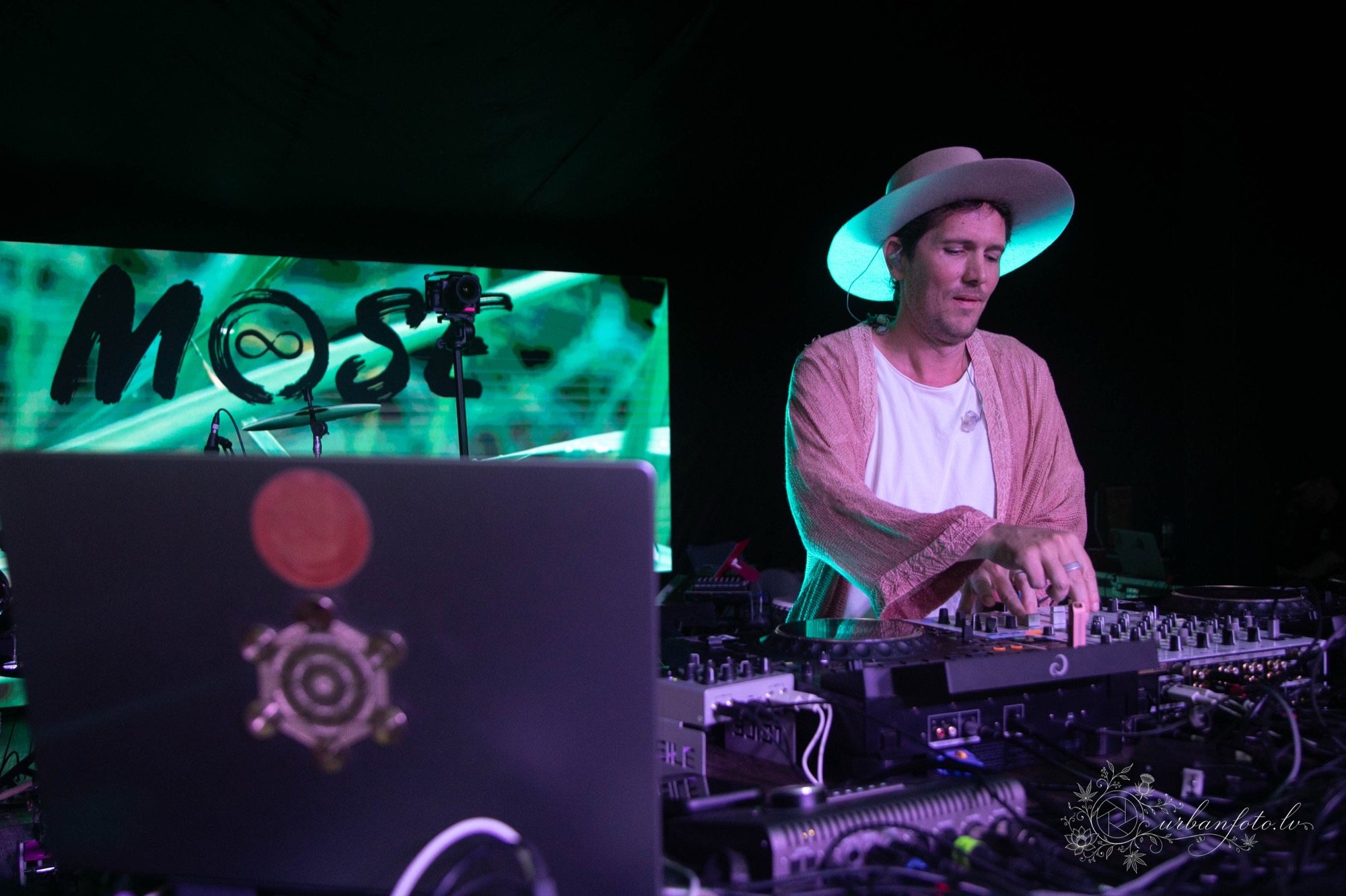 Mose performing a DJ set at BŪTĪBA Festival 2026, mixing electronic music under vibrant turquoise and purple stage lights.