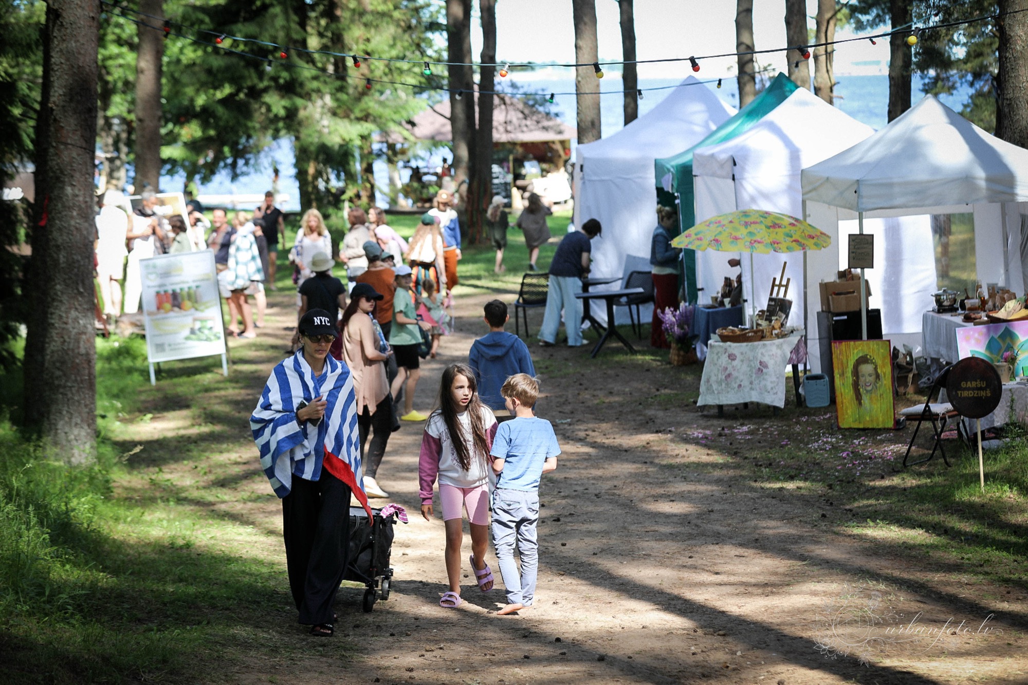 Festival visitors exploring outdoor artisan stalls and market tents along a forest path at BŪTĪBA Festival 2026