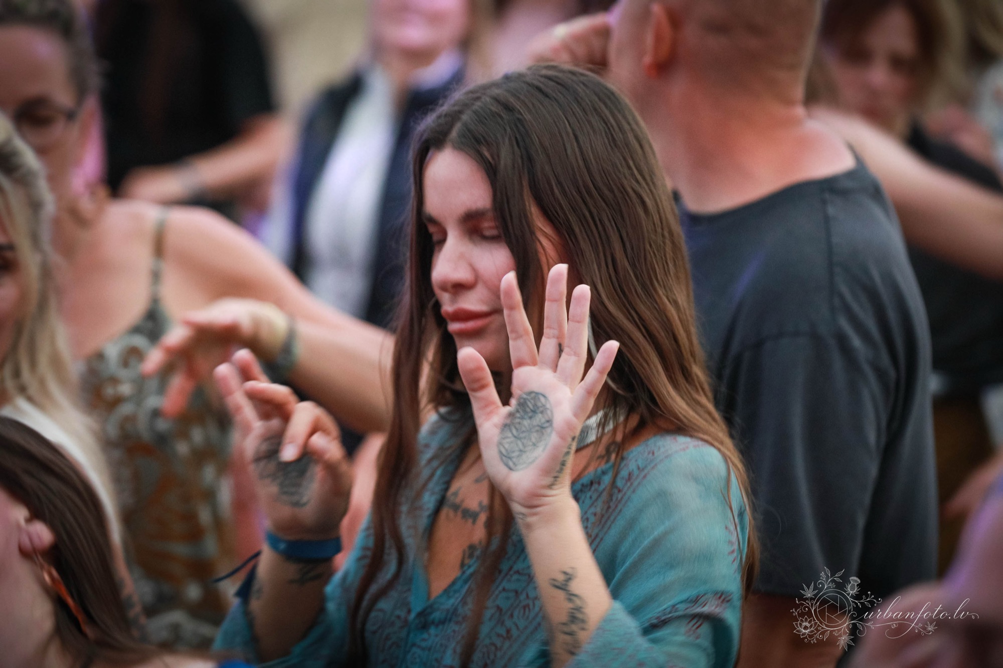 Woman with long dark hair and closed eyes holding up an open, tattooed palm as she dances in the crowd