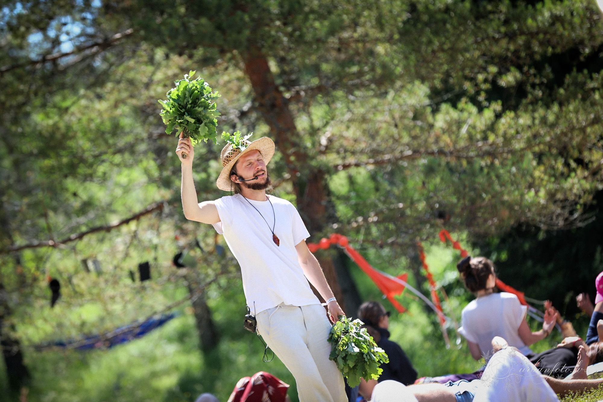 Girts Laube raising a leafy branch during a nature-inspired ritual at BŪTĪBA Festival 2026, surrounded by forest