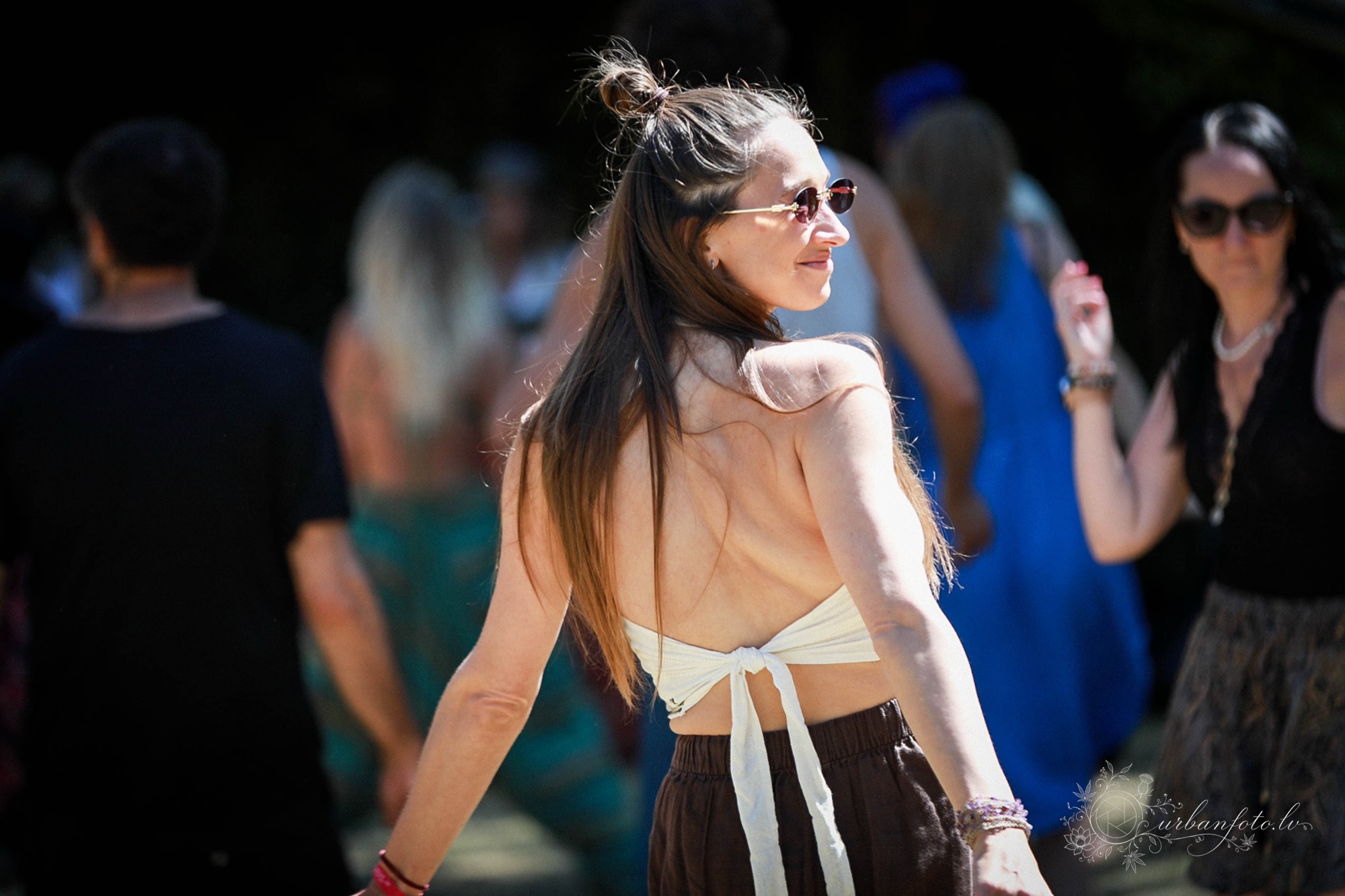 Woman with long hair and sunglasses glancing over her shoulder in the festival crowd at Būtība Festival 2026