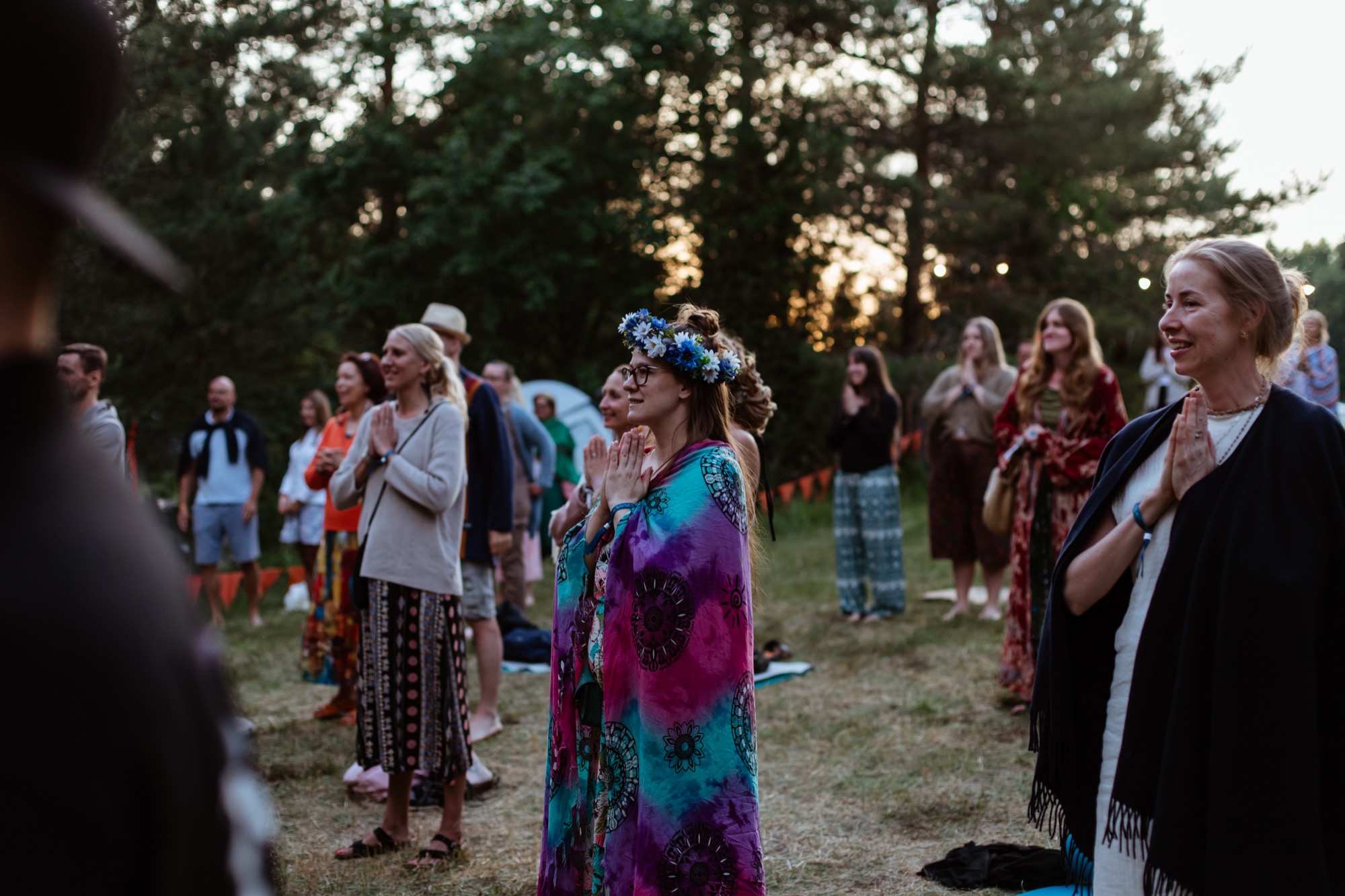 Festival participants standing in a circle in the forest at sunset, with hands held over their hearts during a shared moment of reflection at BŪTĪBA Festival 2026