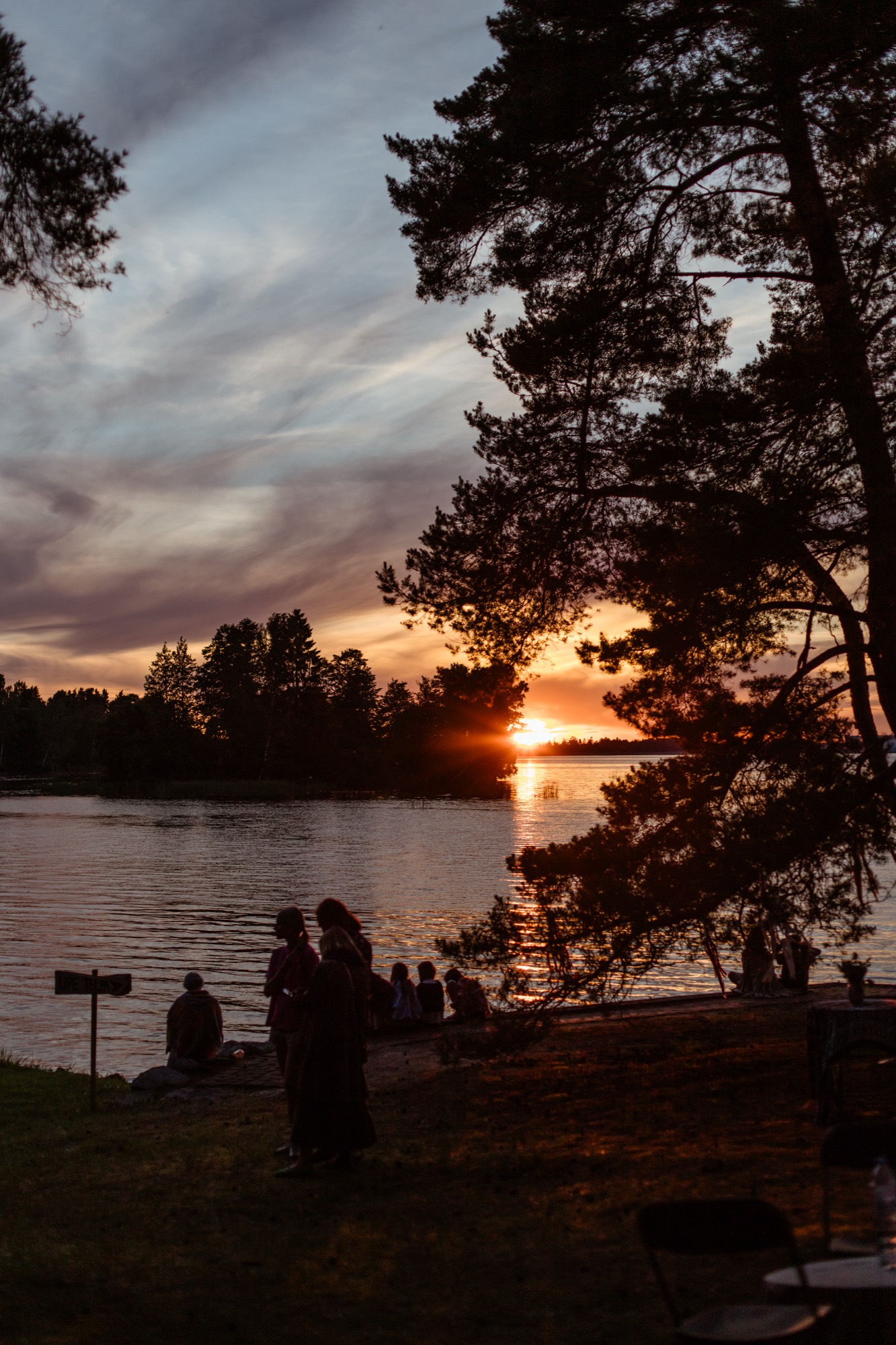 Sunset over the river at BŪTĪBA Festival 2026, with golden light reflecting on the water and pine trees along the shore