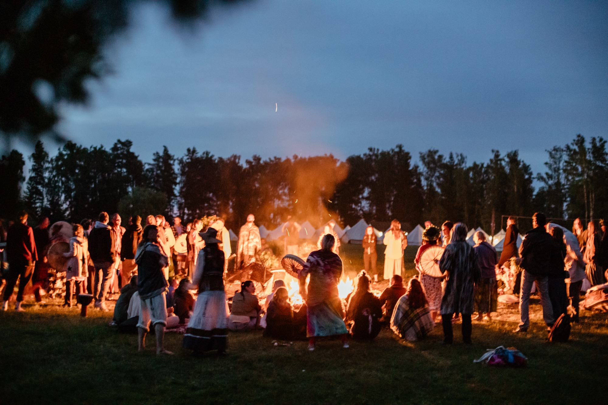 People gathering around a bonfire at BŪTĪBA Festival 2026, sharing music and community beneath the night sky