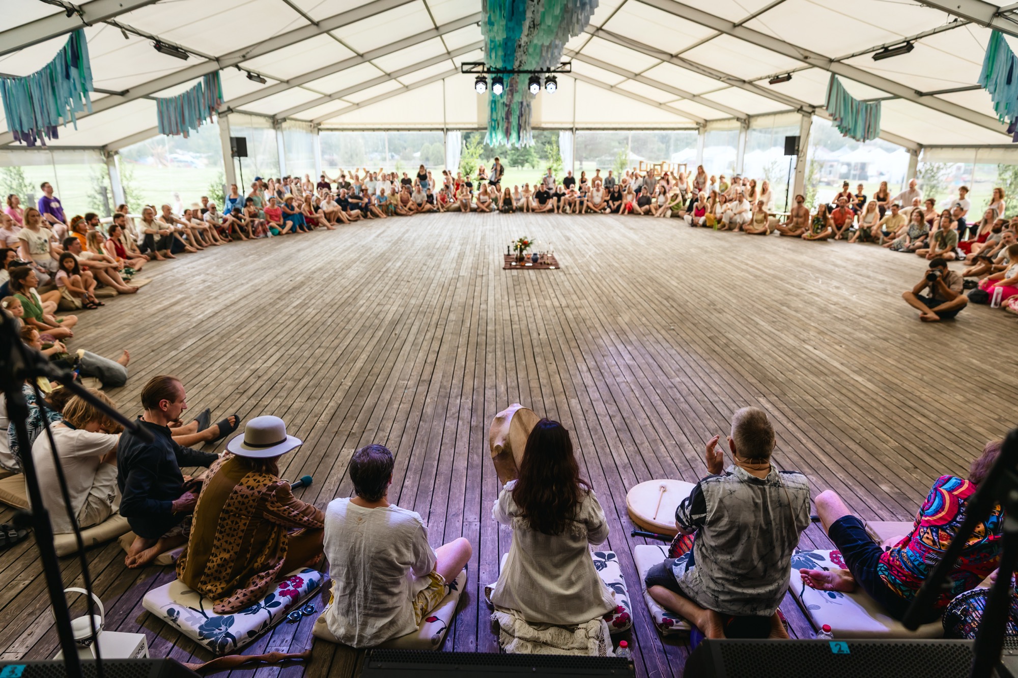 Wide view of festival participants gathered in a circle for a group workshop inside the BŪTĪBA Festival 2026 tent