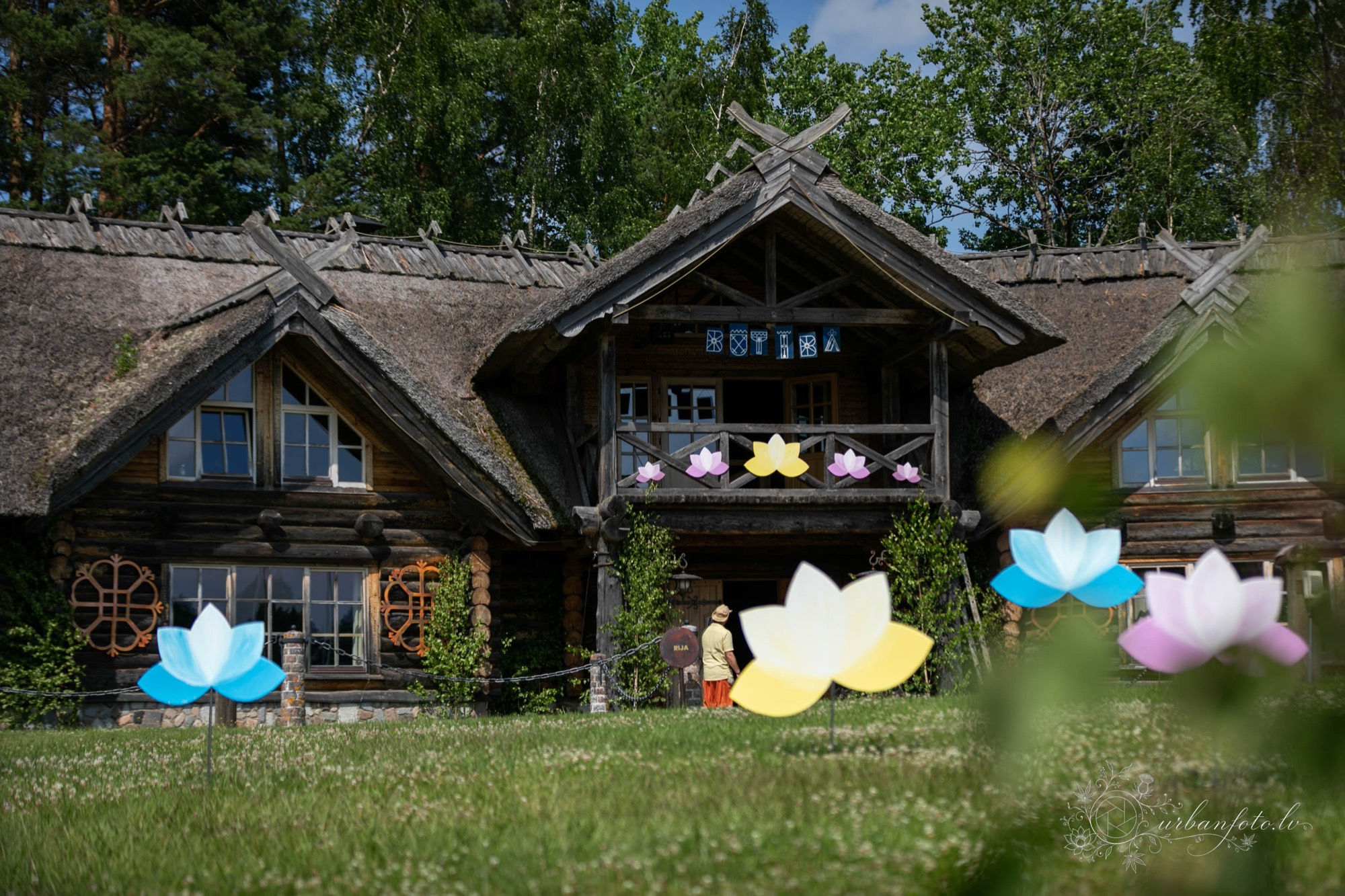 Wooden lodge surrounded by trees and decorated with colourful lotus-shaped ornaments at BŪTĪBA Festival 2026
