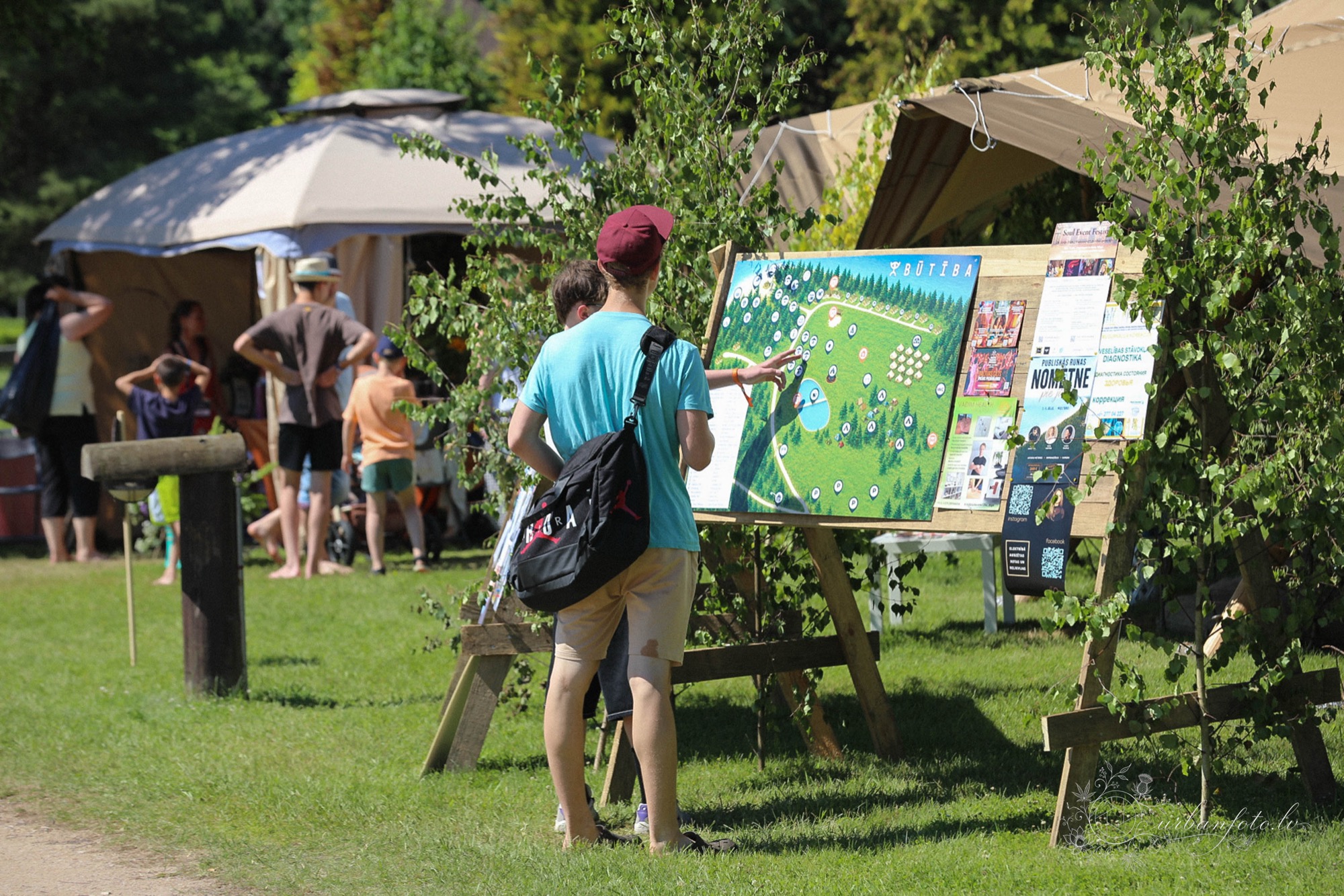 Festival-goer checking the site map and event information board at BŪTĪBA Festival 2026, with tents and greenery in the background