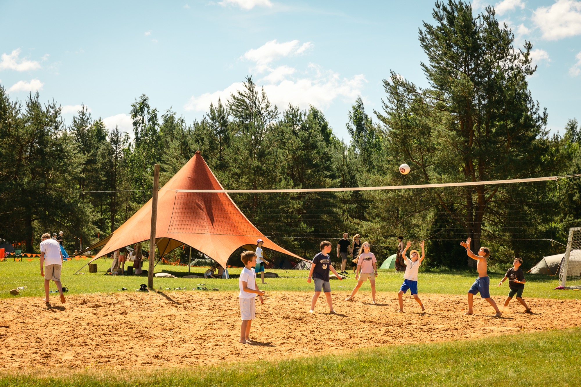 Children playing beach volleyball on a sandy court beneath an orange shade canopy at BŪTĪBA Festival 2026