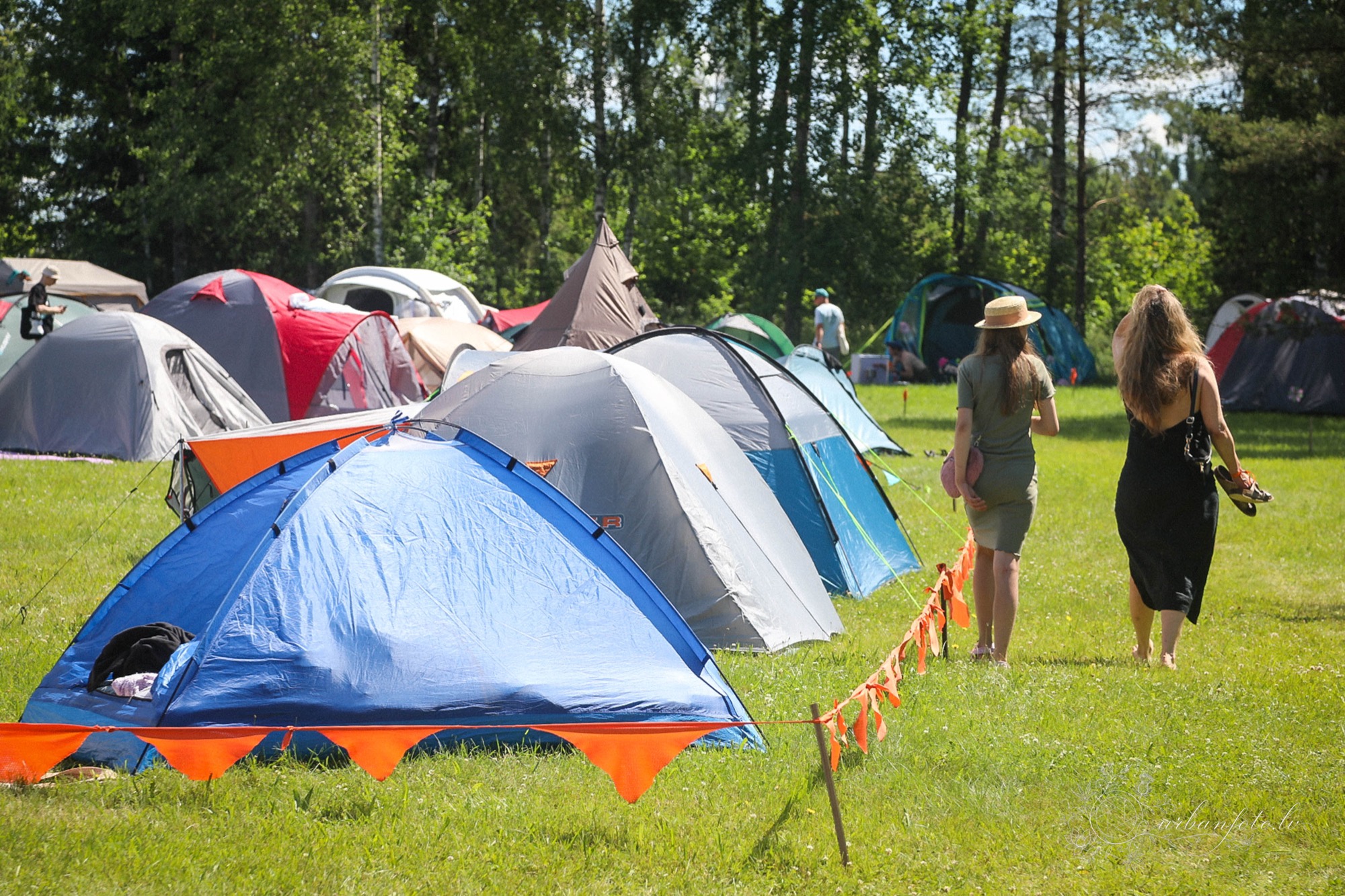 Festival campsite at BŪTĪBA Festival 2026, with colourful tents arranged on a grassy clearing surrounded by forest