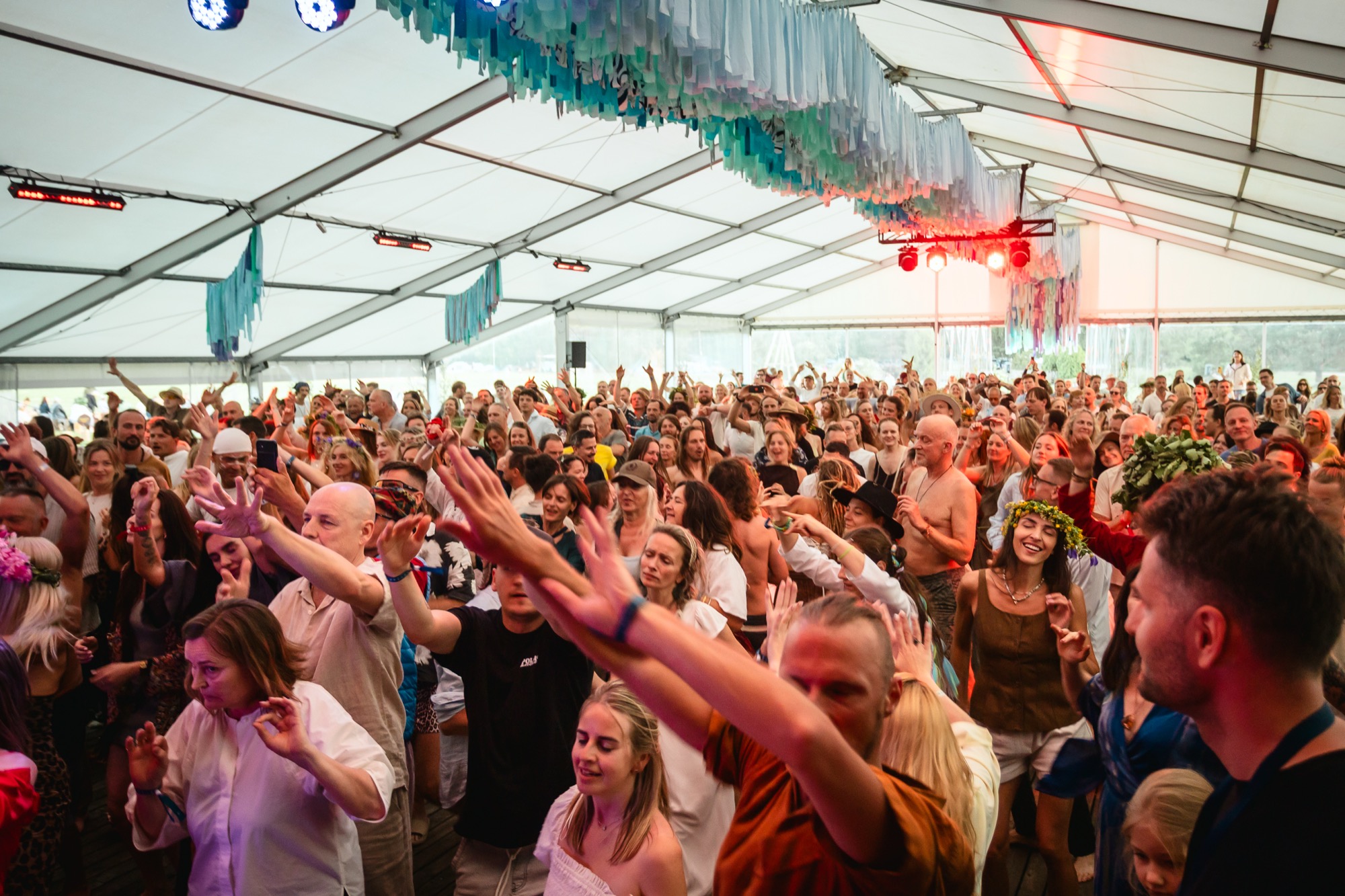 Festival crowd dancing with arms outstretched beneath a festival tent during an energetic ecstatic dance session at BŪTĪBA Festival 2026