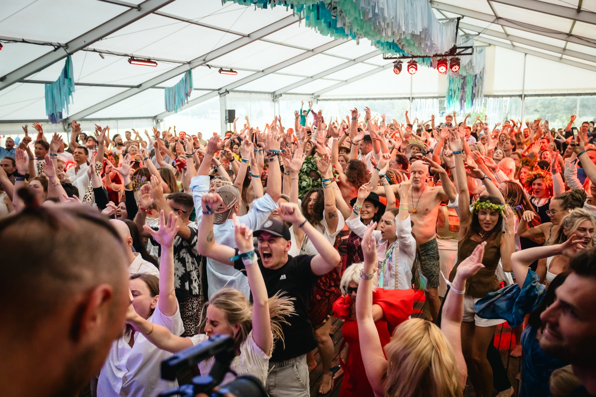 Festival crowd dancing energetically with hands raised during a music and dance session at BŪTĪBA Festival 2026