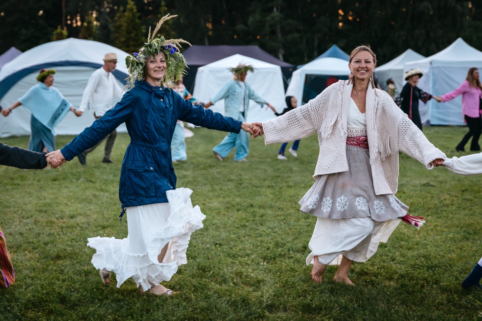 Festival participants holding hands and dancing in a circle on the grass at BŪTĪBA Festival 2026