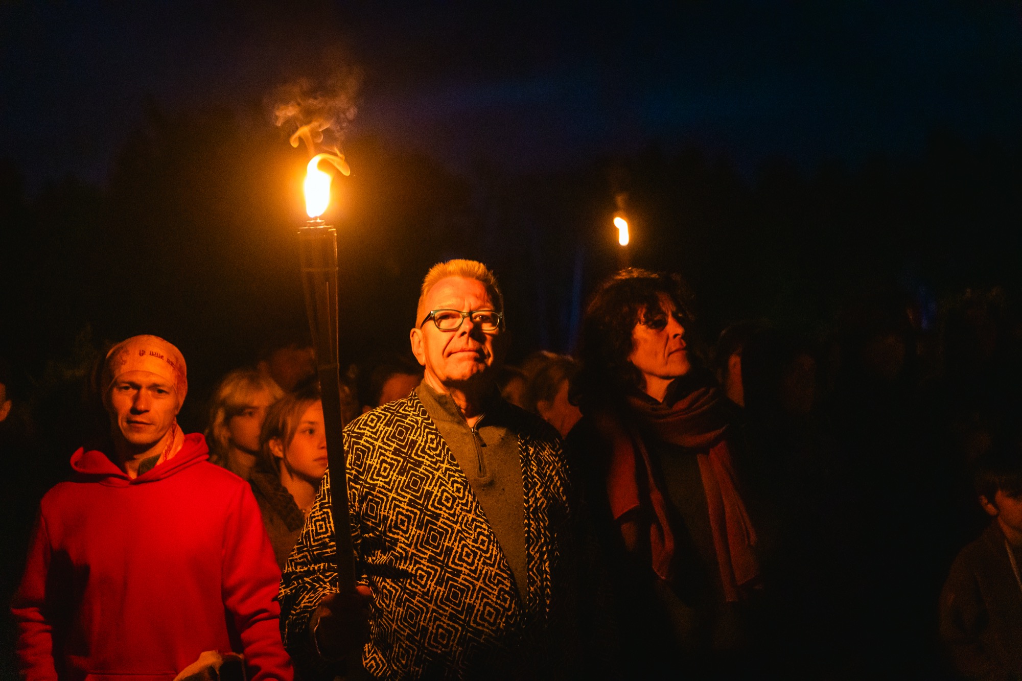 Cilvēki ar lāpām vasaras saulgriežu nakts svinībās BŪTĪBA festivālā, baudot uguns gaismu un kopības sajūtu.