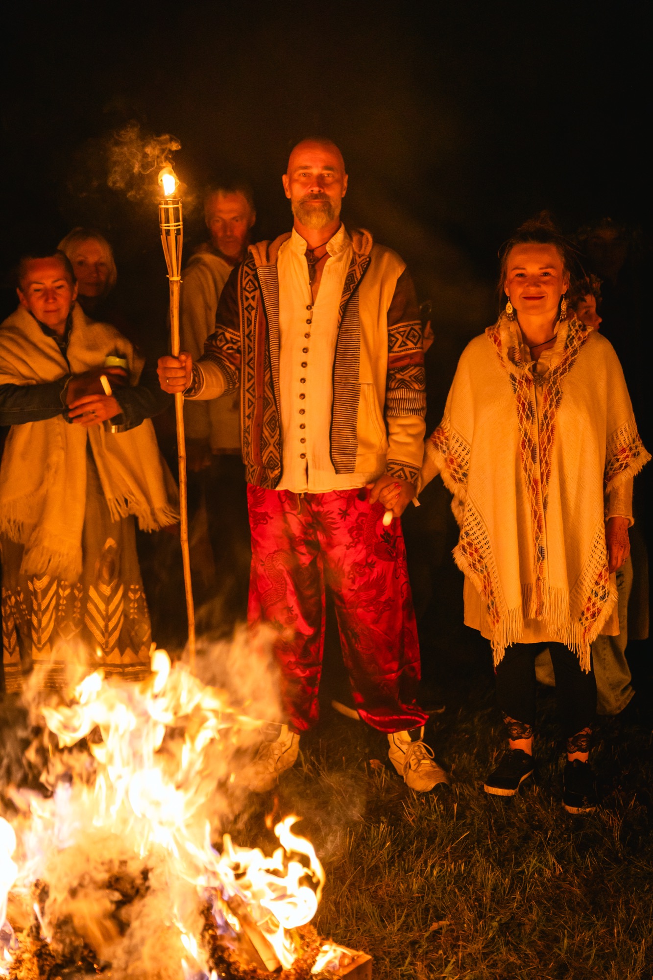 Cilvēki lāpu un ugunskura gaismā svin vasaras saulgriežus BŪTĪBA festivālā, baudot Līgo nakts rituālu noskaņu.