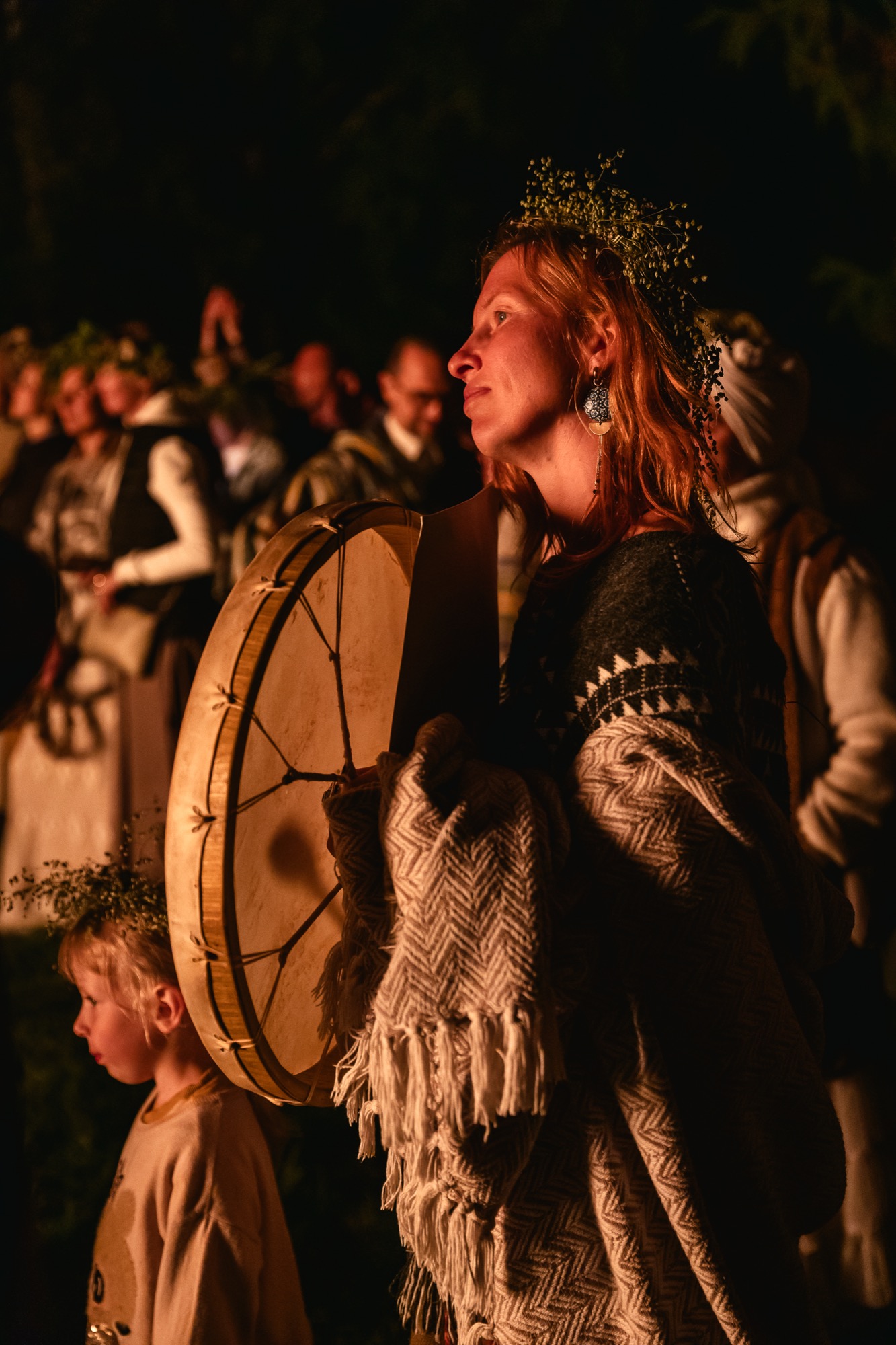 Sieviete ar tradicionālu vainagu un lielu šamaņu bungu BŪTĪBA festivāla nakts svinībās pie ugunskura.