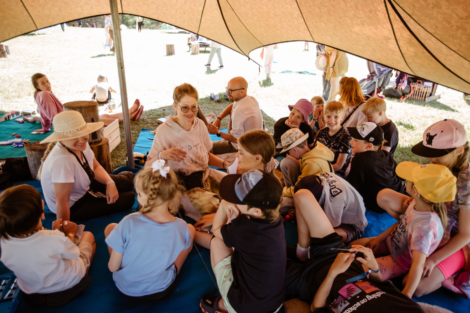 Children taking part in a group workshop under a shaded canopy at BŪTĪBA Festival 2026
