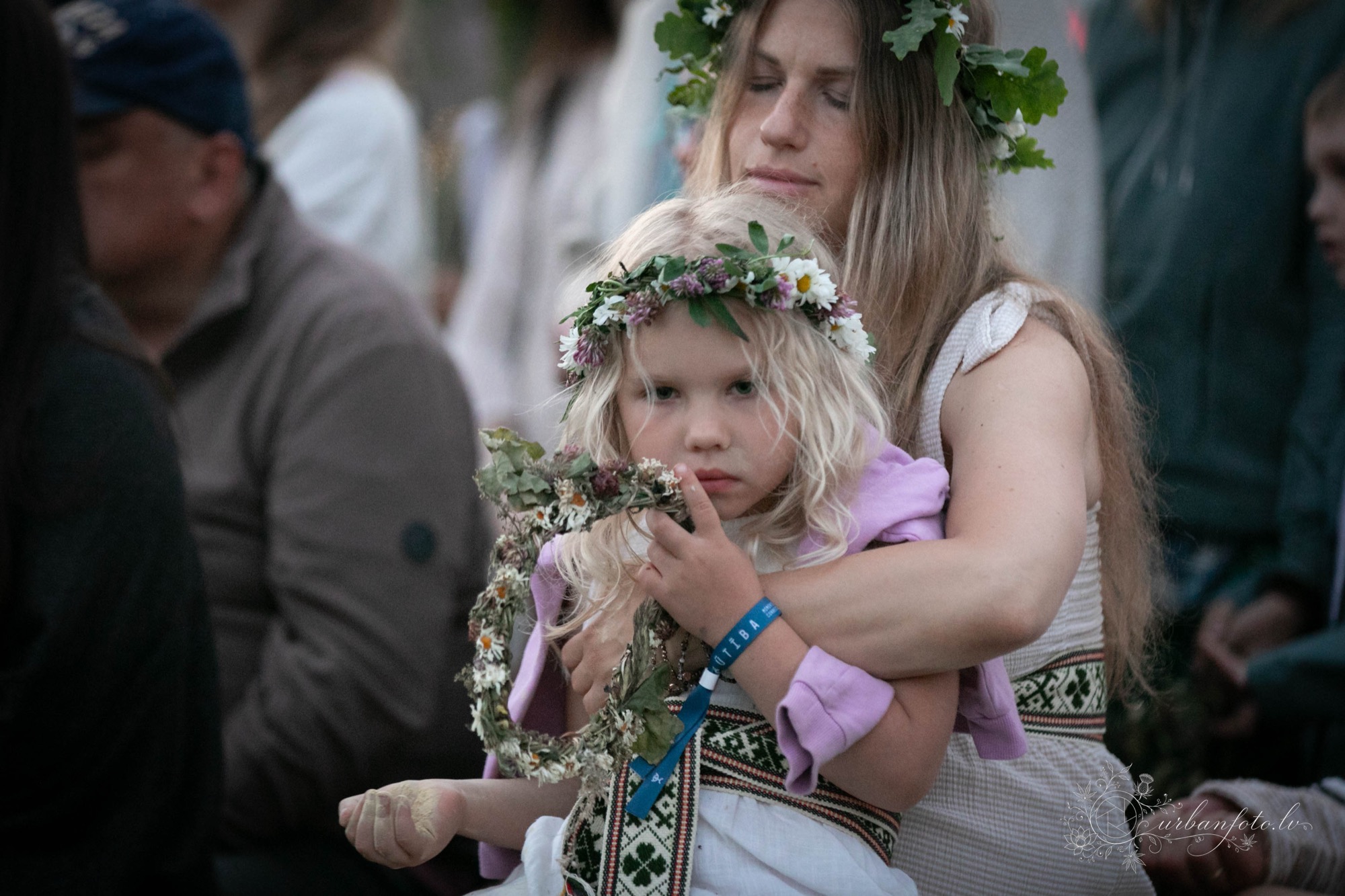Meitene ar Jāņu vainagu rokās kopā ar mammu BŪTĪBA festivāla 2026 vasaras saulgriežu svinībās — ģimenēm draudzīgs festivāls Latvijā.