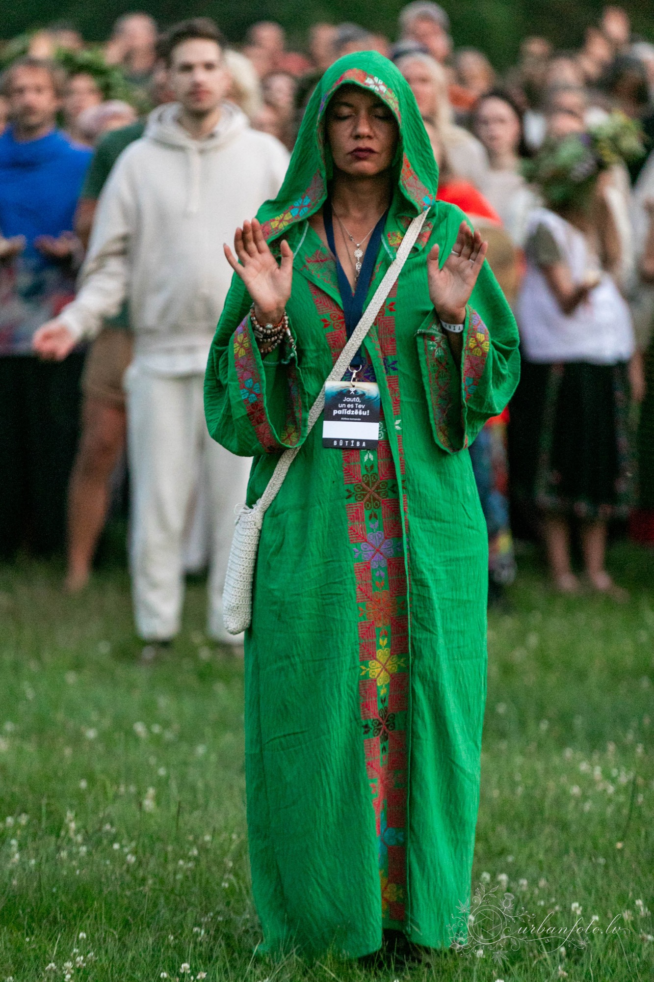 Festival participant in a green embroidered robe with eyes closed and hands raised during a mindful group gathering at BŪTĪBA Festival 2026